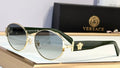 Versace oval sunglasses with gold metal frames, dark green temples, and a signature Medusa logo, displayed on a wooden block with the black branded box in the background.